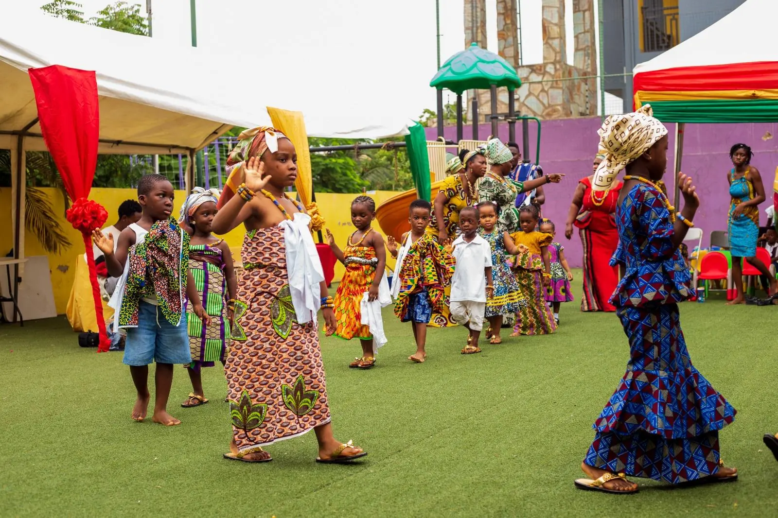 Pupils and adults dancing with raised arms in colourful traditional outfits