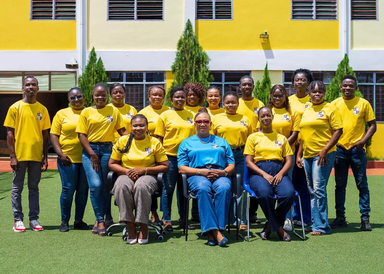 A group in yellow shirts posing with a seated adult outside the HABIS building