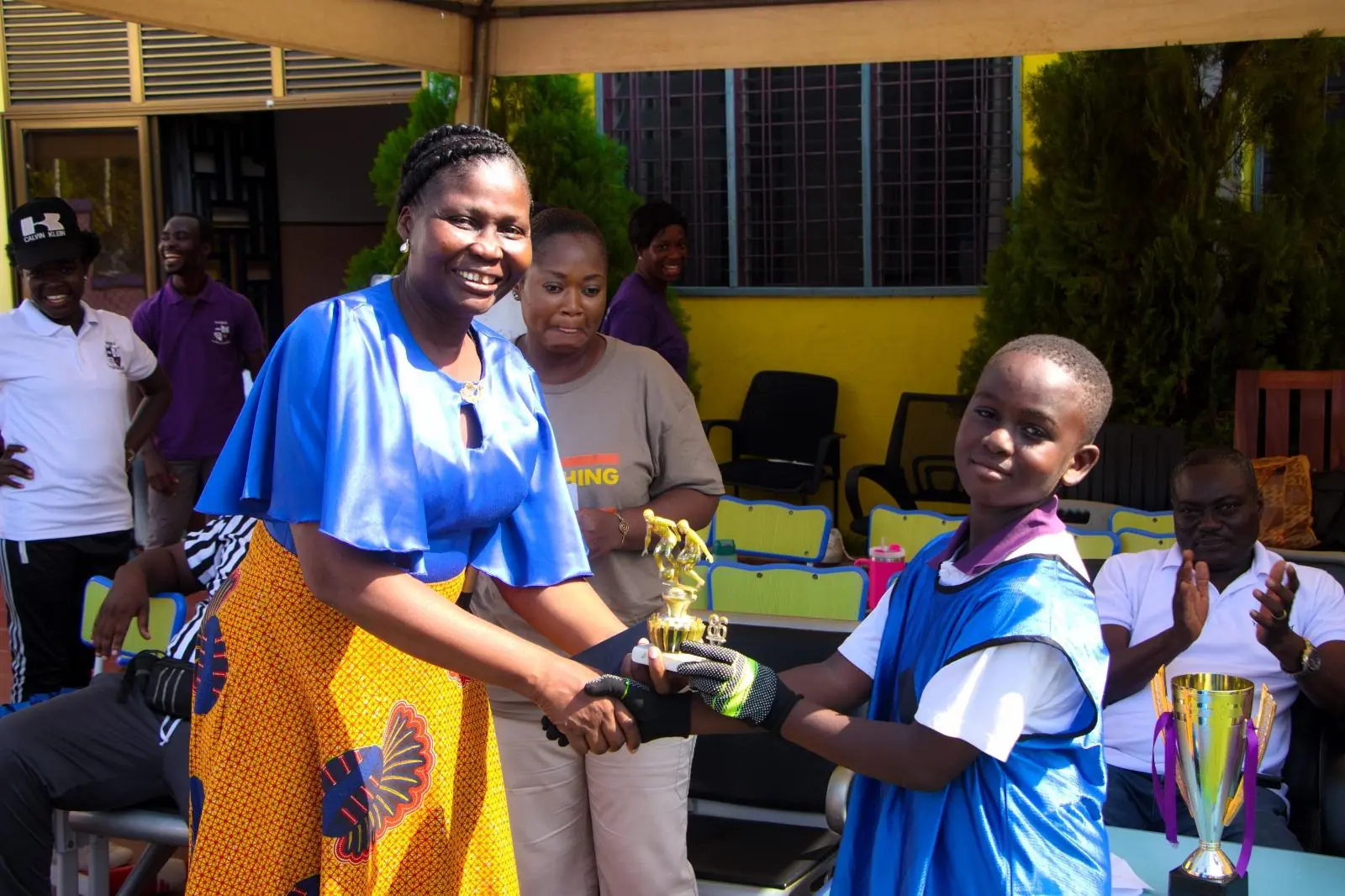 A smiling adult presenting a trophy to a pupil in a blue sports kit